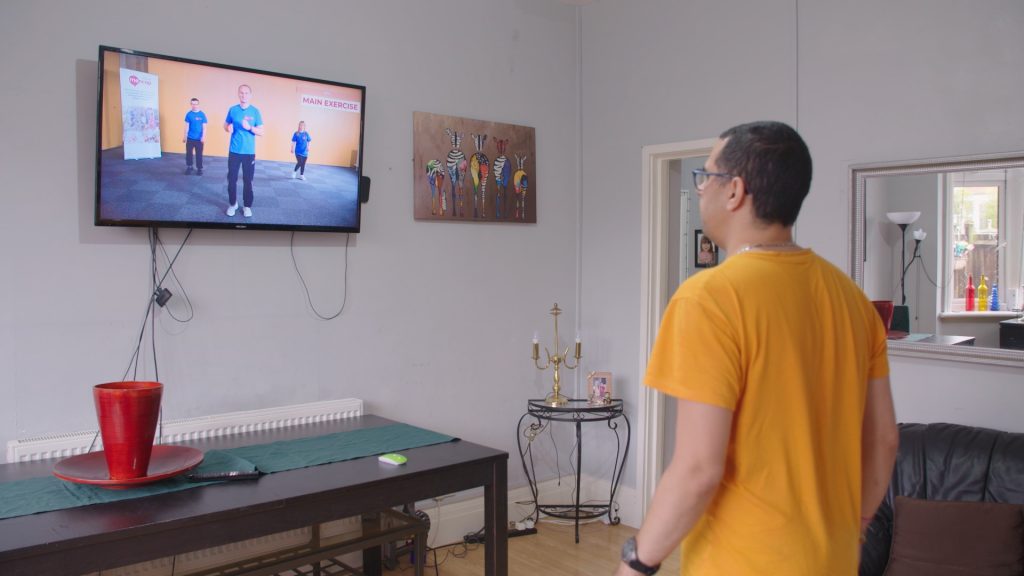 A man exercising at home watching an exercise class for people with a learning disability or autism.