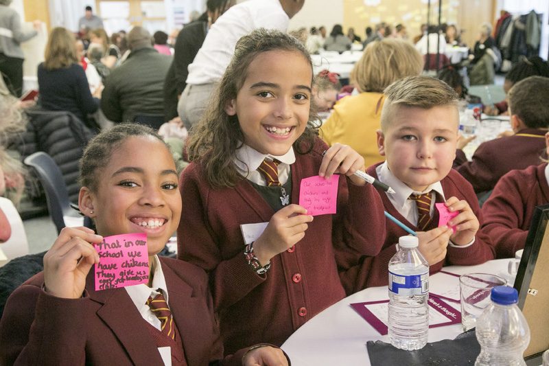 Three children in school uniform at a busy community event in Croydon
