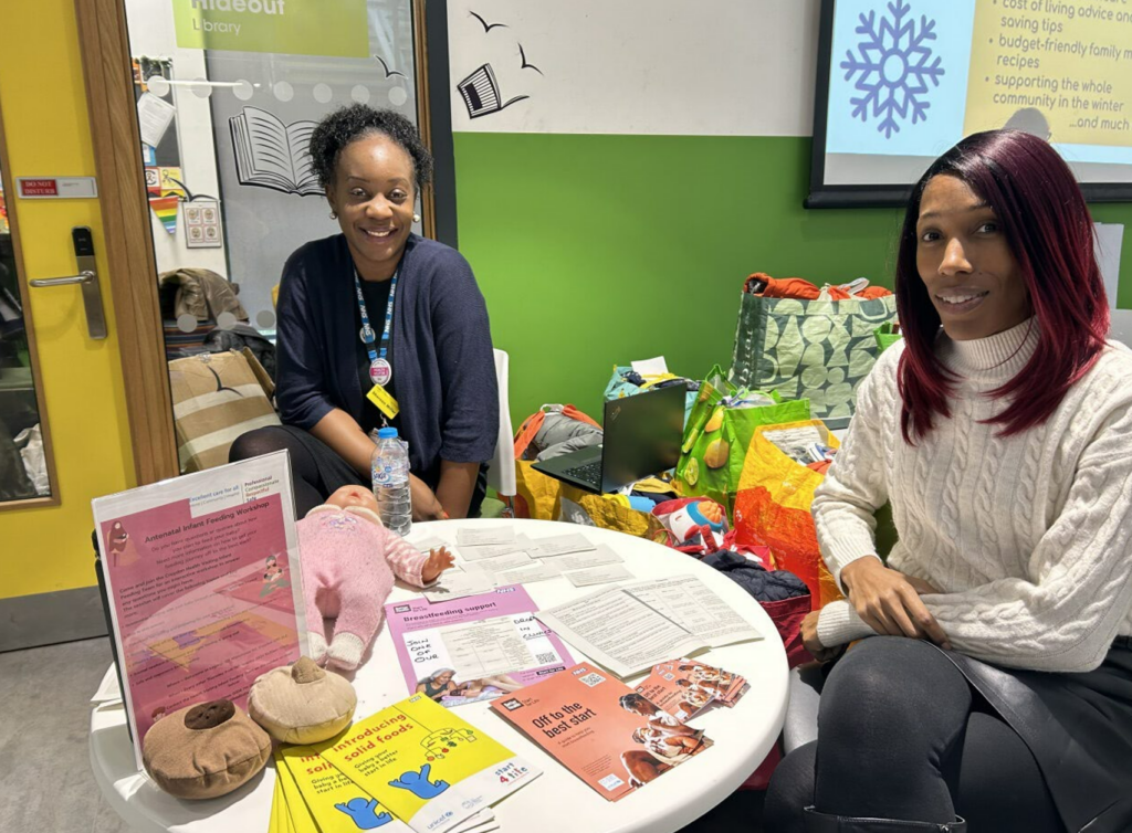 Two female NHS workers sitting at a table which includes leaflets on antenatal support.