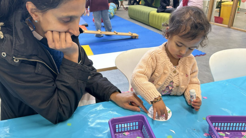 A mum sitting with her young daughter while she does an activity.
