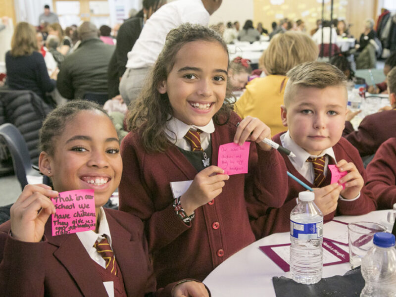 Three children in school uniform at a busy community event in Croydon