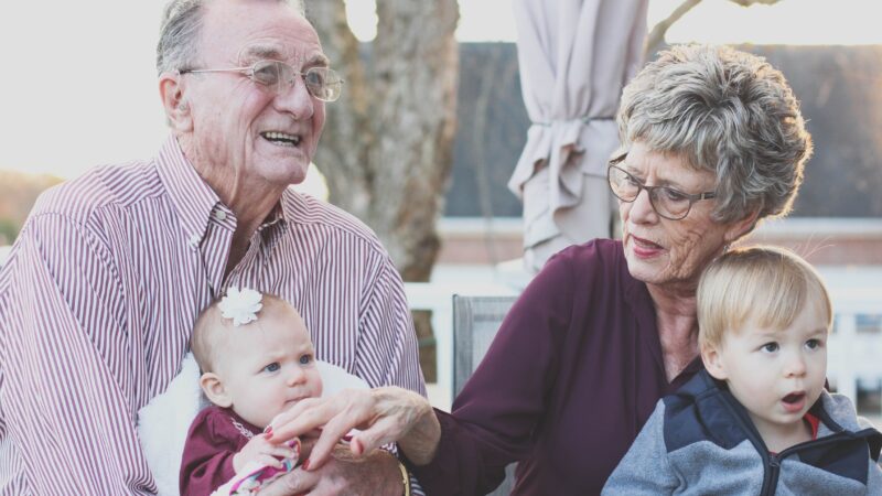 A grandfather and grandmother hold their granddaughter and grandson