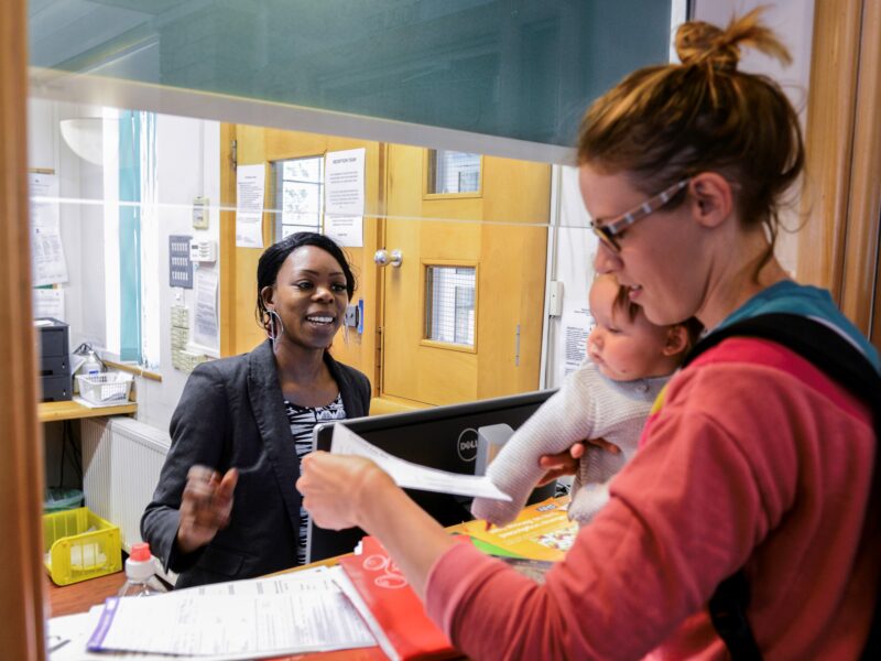 A GP receptionist talking to a mother and her baby