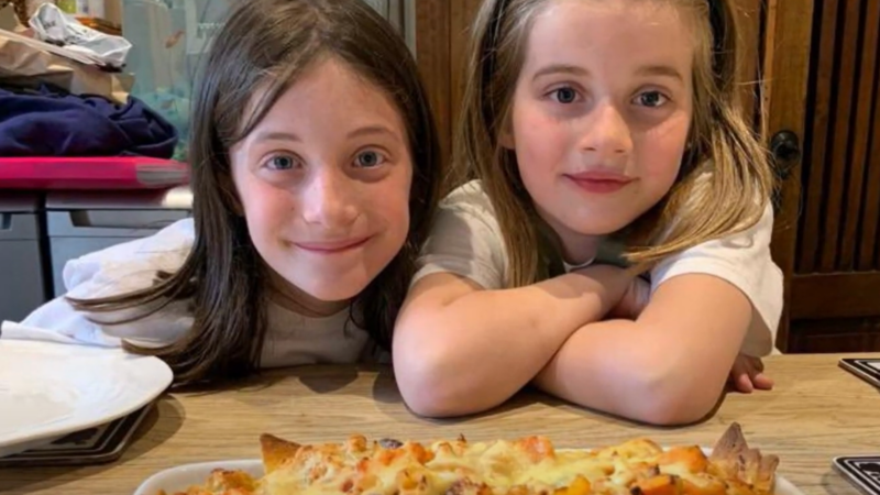 Two young girls sitting at a dinner table looking proudly at the meal they have made