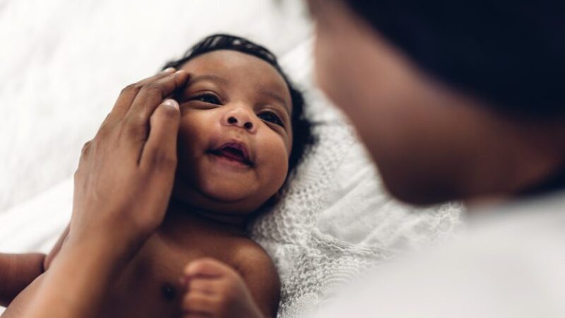 A new born baby looking up at its mother's face as she holds it in her arms