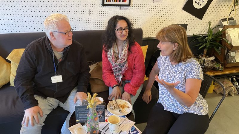 A man talking with two women over a cup of coffee at Merton's Memory Cafe